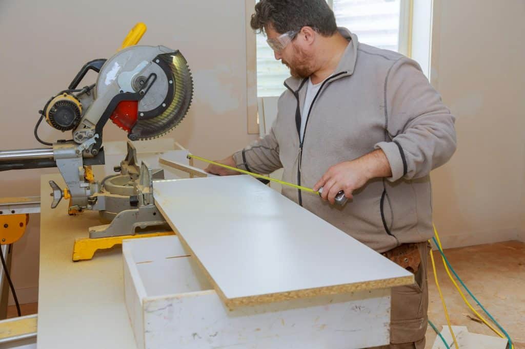 Workers installing laminate and measuring tape laminated white shelves before cutting