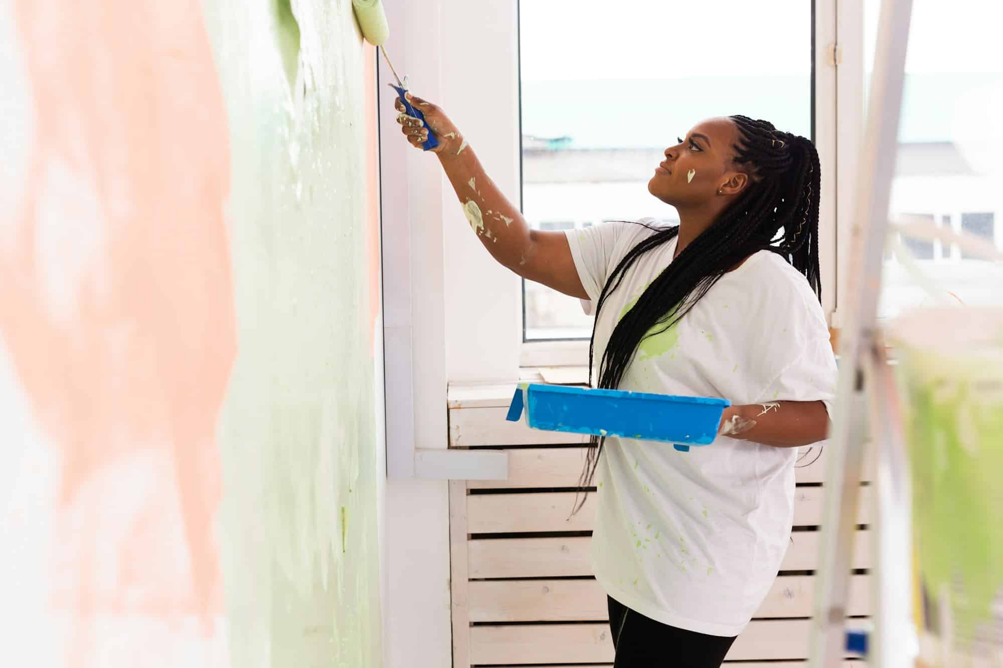 Afro woman painting the walls of new home. Renovation, repair and redecoration concept