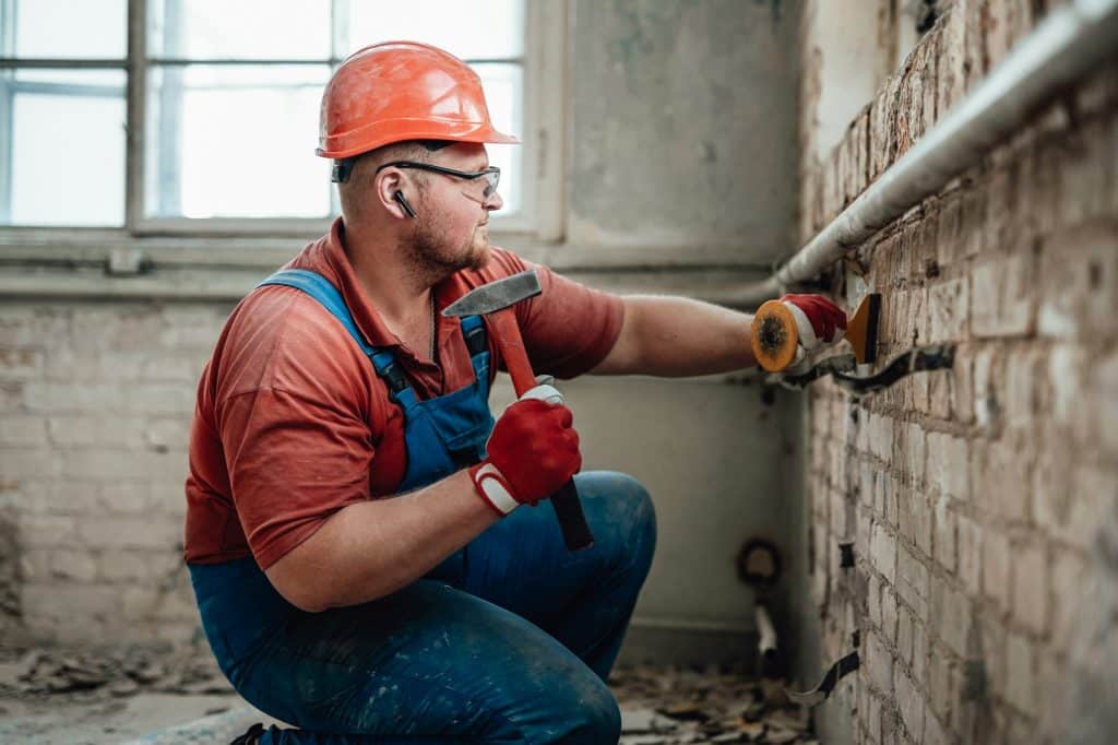 Concentrated builder on a construction site working on a brick wall with a hammer