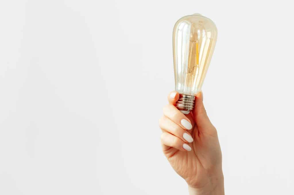 Female hand holding light bulb against gray background