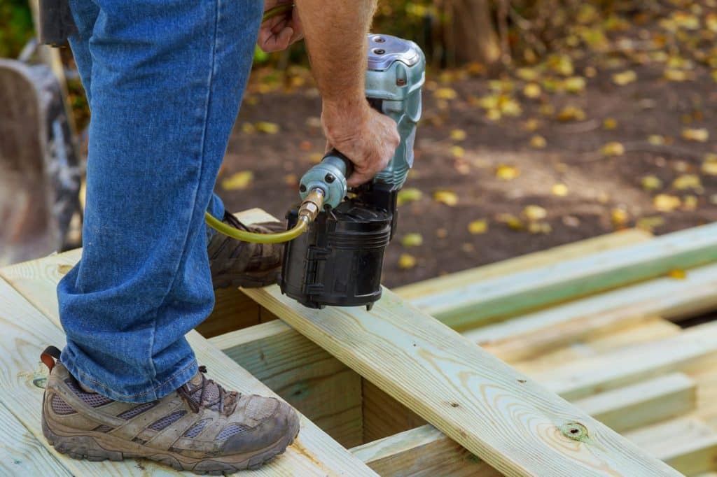 Handyman installing wooden flooring in patio, working using nail gun to nail