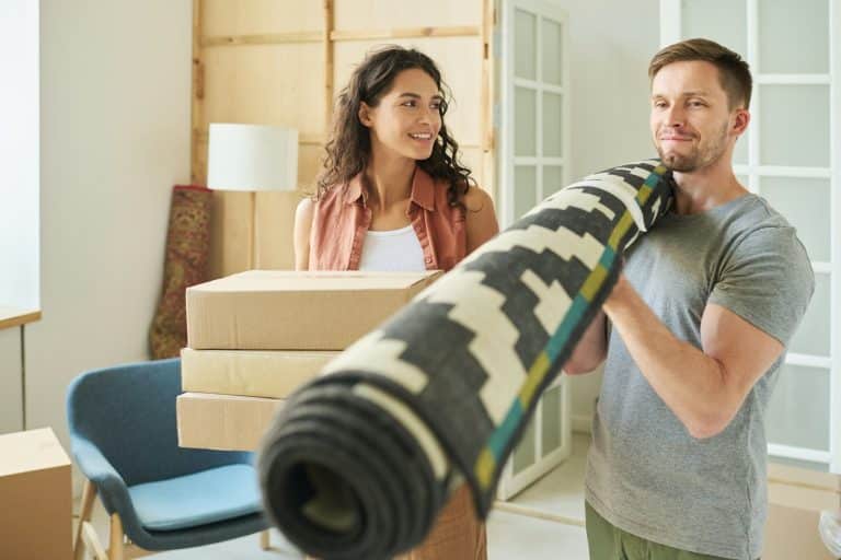 Happy young man holding rolled carpet on his shoulder while carrying it