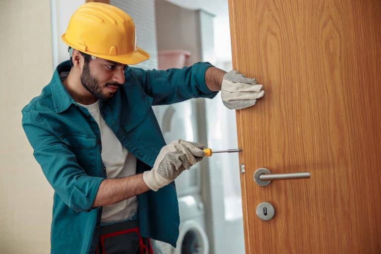 Locksmith workman in uniform installing door knob. Professional repair service