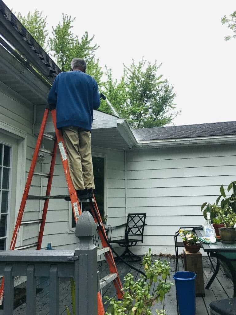 Man on ladder cleaning gutters on roof