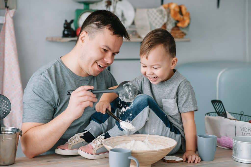 Young man and his son with oven sheet in kitchen. Father with little son on the kitchen