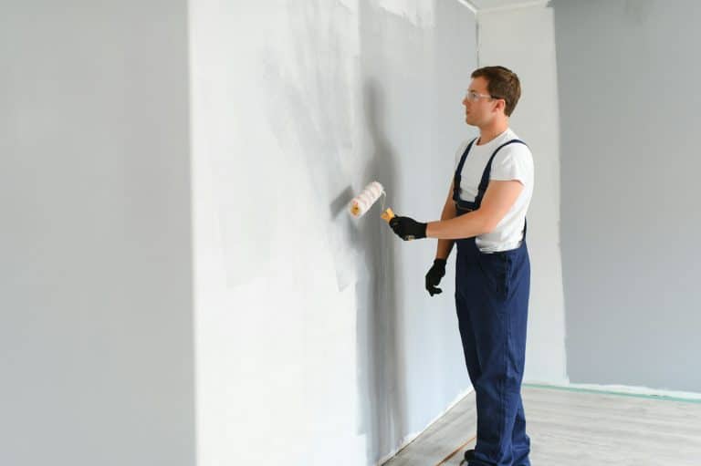 Young worker painting wall in room