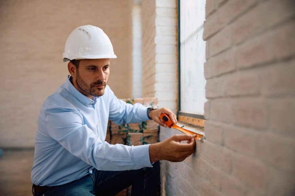 Building contractor using measuring tape at construction site.