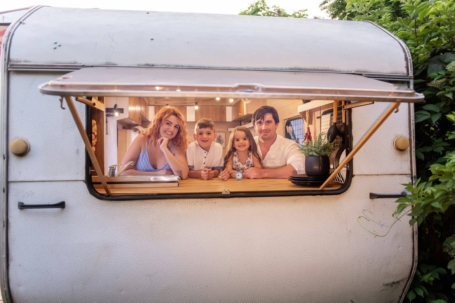 Cheerful family of travelers look out from mobile home, trailer house. People are having fun